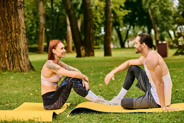 A en ropa deportiva sentarse en una alfombra en el parque, dirigido por un entrenador personal, mostrando determinación y motivación. - foto de stock