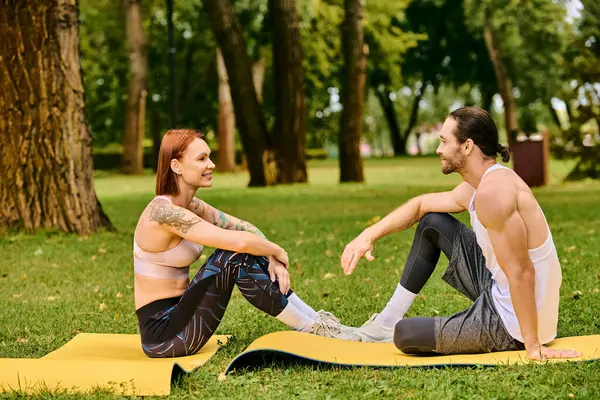 A in sportswear sit on a mat in the park, led by a personal trainer, displaying determination and motivation. — Stock Photo