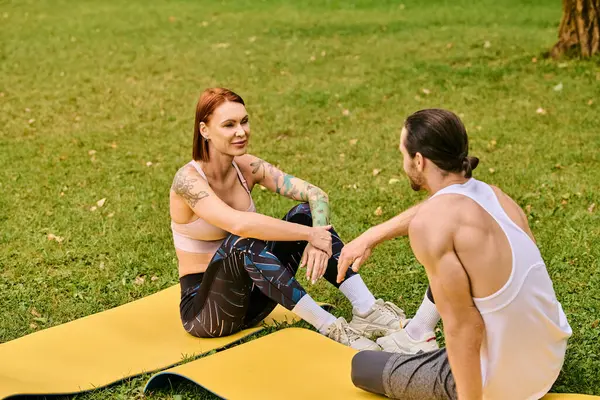 Uma mulher, vestida de sportswear, participando de uma sessão de treino guiada por um personal trainer em um tapete no parque. — Fotografia de Stock