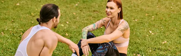 Un uomo e una donna in abbigliamento sportivo siedono insieme sull'erba, uniti nel loro percorso di fitness. Essi trasudano determinazione e motivazione. — Foto stock