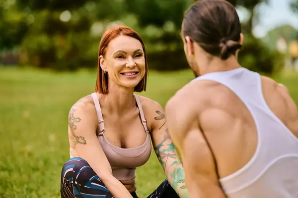 A determined woman in sportswear sits on the ground next to a man, both immersed in their outdoor exercise routine, led by a personal trainer. — Stock Photo