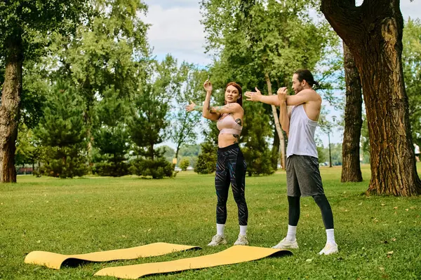 Un hombre y una mujer en ropa deportiva practican yoga posan con determinación y motivación en un entorno sereno del parque. - foto de stock