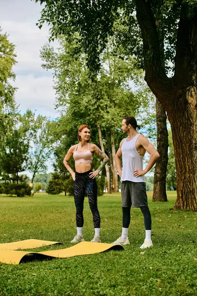 Una donna in stand di abbigliamento sportivo impegnata in una routine di fitness con personal trainer in un ambiente parco sereno. — Foto stock