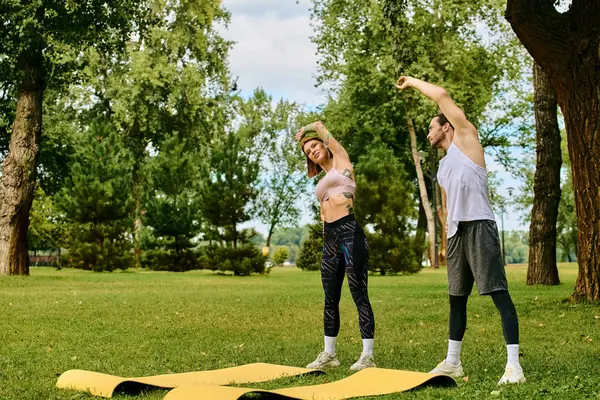 Un uomo e una donna determinati, sia in abbigliamento sportivo, praticare in un ambiente parco sereno, sotto la guida di un personal trainer. — Foto stock