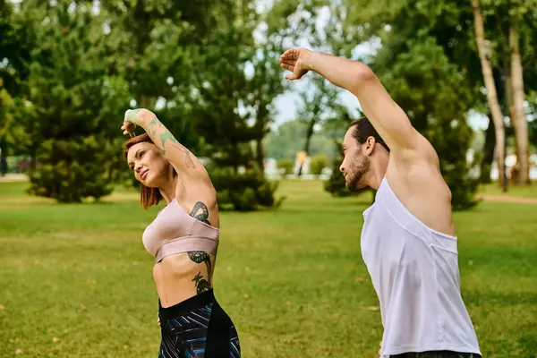 A man and a woman in sportswear performing yoga poses together in a serene park setting — Stock Photo