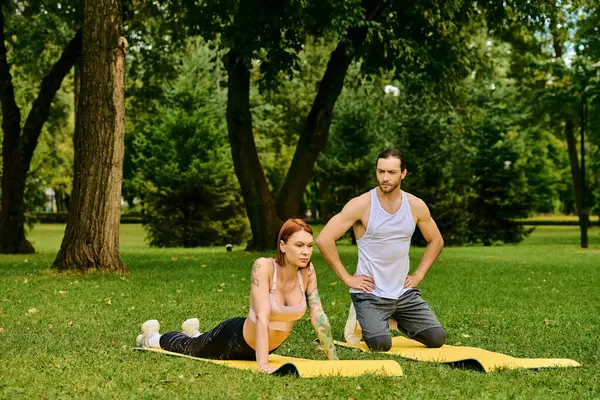 Una donna in abbigliamento sportivo pratica yoga posa in un parco lussureggiante guidato da un personal trainer, incarnando determinazione e motivazione. — Foto stock
