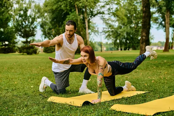 Una donna in abbigliamento sportivo pratica yoga insieme sotto il cielo aperto, guidata da un personal trainer. — Foto stock