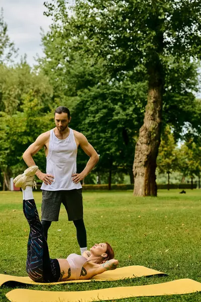 A woman in sportswear, guided by a personal trainer, practice yoga poses with determination and motivation in a serene park. — Stock Photo
