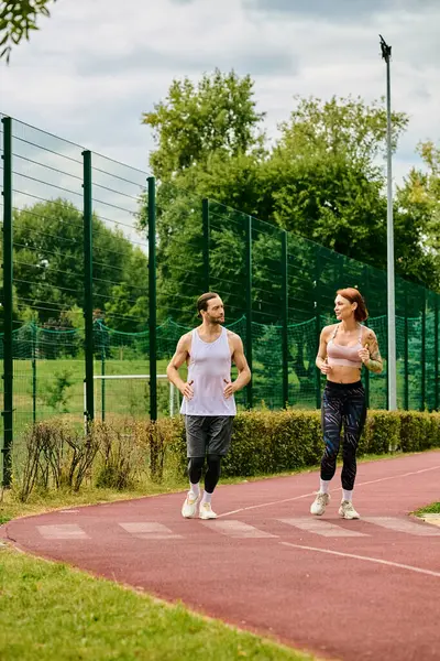 A woman in sportswear, led by a personal trainer, sprinting with determination and motivation on a track. — Stock Photo