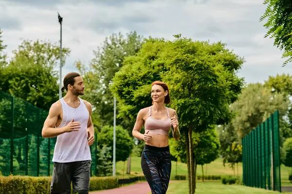 Un hombre y una mujer en ropa deportiva, corriendo juntos en un parque, alimentados por la determinación y la motivación - foto de stock