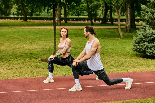 Una donna dedicata nello sport di pratica dell'abbigliamento sportivo con determinazione guidata dal proprio personal trainer in un tranquillo parco. — Foto stock