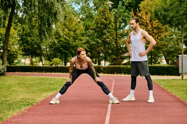 A woman in sportswear, guided by their personal trainer, display determination and motivation while stretching outdoors in a serene park setting. — Stock Photo