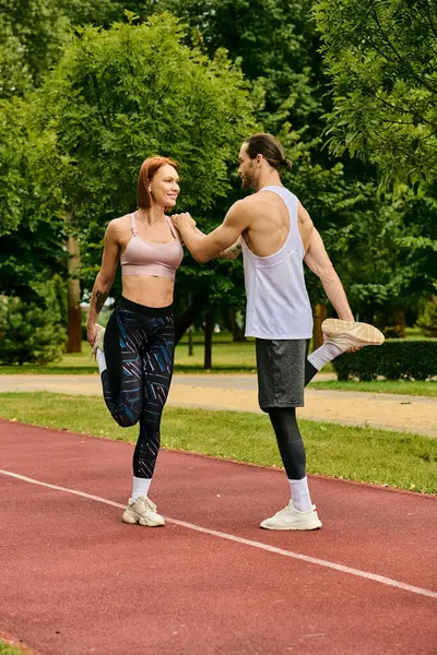 Un hombre y una mujer en ropa deportiva que se extienden lado a lado en una pista, mostrando determinación y motivación hacia sus objetivos de fitness. - foto de stock