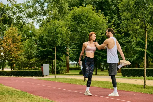 Un hombre y una mujer en ropa deportiva que se extienden juntos en un sendero del parque. Su determinación y motivación brillan a través. - foto de stock
