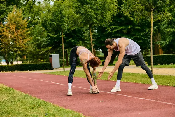 Una mujer decidida en ropa deportiva, guiada por un entrenador personal, están haciendo ejercicio juntos en una pista. - foto de stock