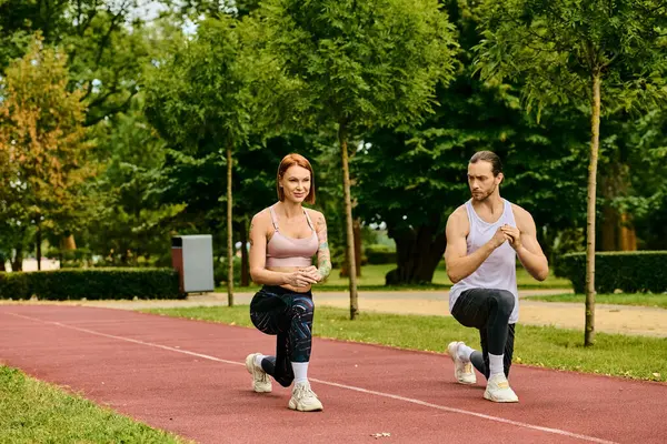 Чоловік і жінка в спортивному одязі беруть участь в синхронізованих присіданнях в парку Їх рішучість і мотивація очевидні. — стокове фото