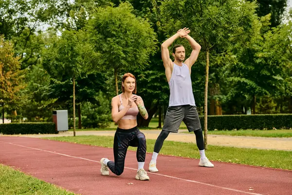 Un entrenador personal guía a una mujer mientras hacen ejercicio juntos en una pista, mostrando determinación y motivación. - foto de stock