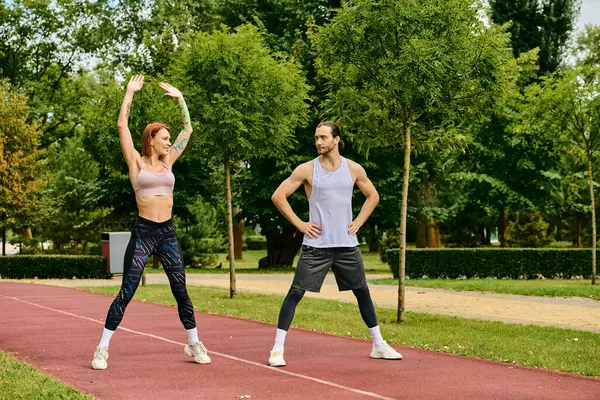 Un hombre y una mujer decididos en ropa deportiva, entrenan juntos en una pista, mostrando motivación y trabajo en equipo. - foto de stock