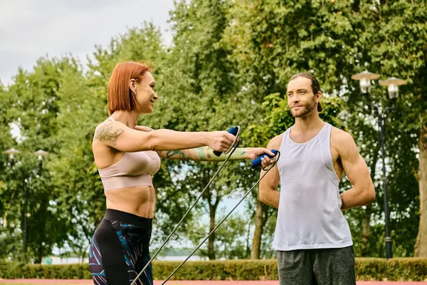Una mujer en ropa deportiva que hace ejercicio al aire libre con un entrenador personal, mostrando determinación y motivación. - foto de stock