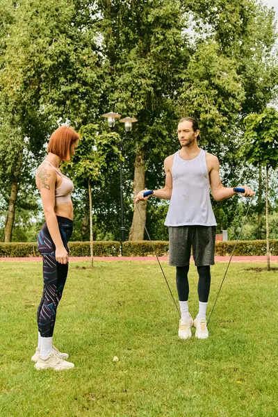 A man and a woman in sportswear stand atop a vibrant green field, showcasing their determination and motivation during an outdoor workout together. — Stock Photo