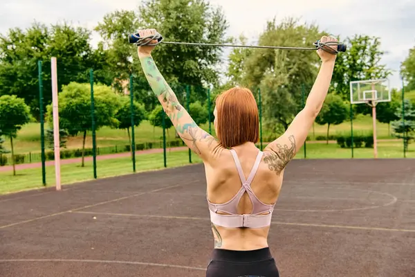 Una donna determinata in abbigliamento sportivo che tiene una corda da salto in un parco, incarnando motivazione e forza. — Foto stock