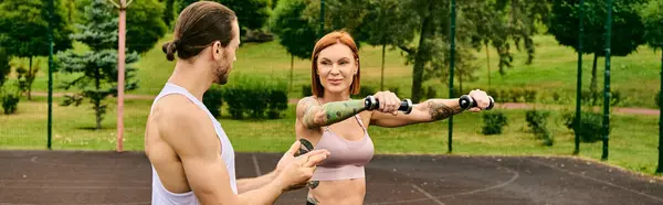 A determined woman in a bra top is holding a dumbbell outdoors, showing motivation and strength during an exercise session led by a personal trainer. — Stock Photo