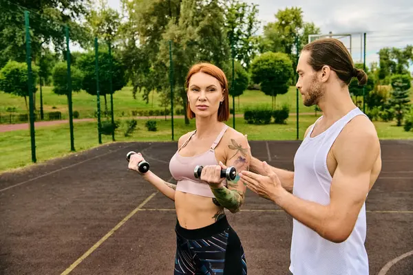 Un hombre y una mujer decididos en ropa deportiva haciendo ejercicio junto con pesas afuera - foto de stock