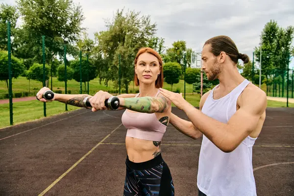 Un hombre y una mujer decididos en ropa deportiva haciendo ejercicio con pesas - foto de stock