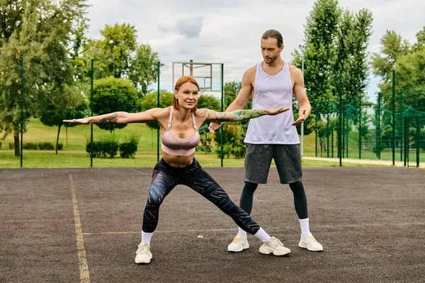 Un hombre y una mujer en ropa deportiva se paran en una cancha de tenis, centrándose en su entrenamiento con determinación y motivación. - foto de stock