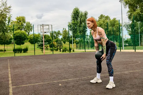 Una mujer decidida sosteniendo una pelota en una pista vibrante, atleta en ropa deportiva. - foto de stock