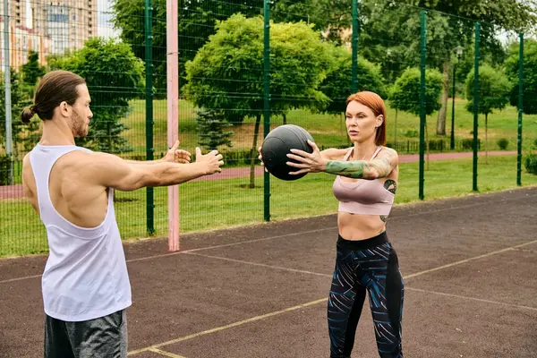 Un hombre y una mujer en ropa deportiva se ejercitan juguetonamente con una pelota al aire libre, mostrando determinación y motivación. - foto de stock