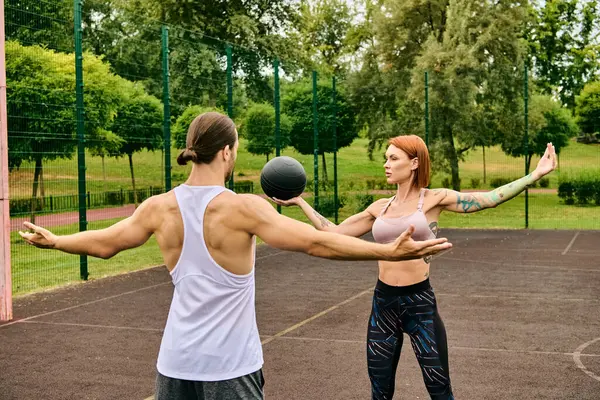 Мужчина и женщина в спортивной форме игриво играют в мяч на открытом воздухе, воплощая решимость и мотивацию с личным тренером. — стоковое фото