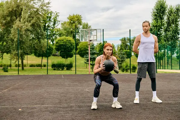 A determined man and woman in sportswear workout on an outdoor court under the guidance of a personal trainer. — Stock Photo