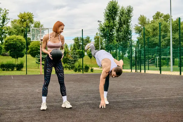 Решительная женщина бросает вызов гравитации мячом, демонстрируя силу и равновесие, пока ее личный тренер наблюдает. — стоковое фото