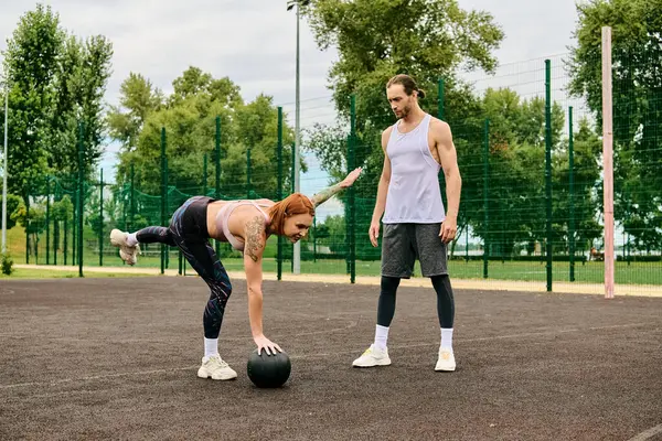 Uma mulher em sportswear desfrutar de um momento lúdico, exercitando ao ar livre com uma bola sob a orientação de um personal trainer. — Fotografia de Stock