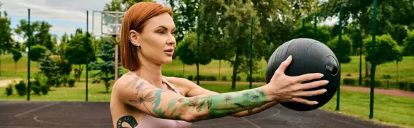 A woman in sportswear, holding a medicine ball, trains outdoors with determination — Stock Photo