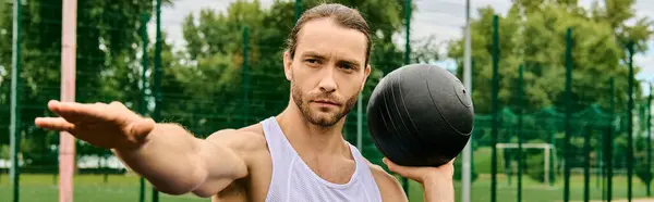 Ein Mann in Sportbekleidung, der einen schwarzen Ball in der rechten Hand hält, konzentriert sich auf seine Outdoor-Übung. — Stockfoto