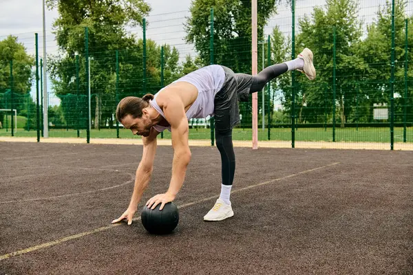 Un homme en vêtements de sport montre ses compétences en effectuant un tour sur une balle dans une séance d'exercice en plein air dirigée par un entraîneur personnel. — Photo de stock