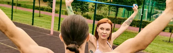 Una mujer decidida se para frente a una cancha en ropa deportiva, lista para una sesión de entrenamiento con su entrenador personal. - foto de stock
