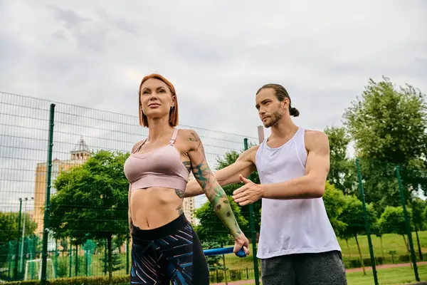 Un homme et une femme, vêtus de vêtements de sport, debout sur un court de tennis, prêts pour un entraînement stimulant avec un entraîneur personnel. — Photo de stock