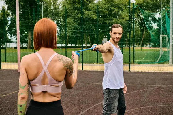 A man in sportswear holds a resistance band while standing next to a determined woman — Stock Photo