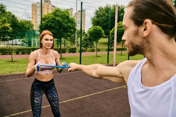 Un hombre y una mujer, ambos en ropa deportiva, sosteniendo banda de resistencia y practicando al aire libre - foto de stock