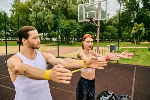 A man and a woman in sportswear having resistance band training with determination and motivation outdoors. — Stock Photo