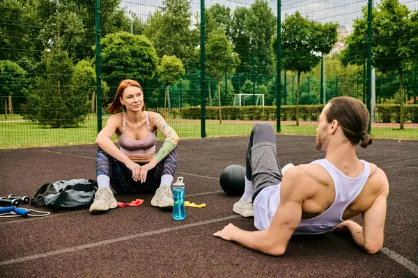 Un hombre y una mujer en ropa deportiva se sientan en una cancha de baloncesto, compartiendo determinación y motivación mientras hacen ejercicio juntos.. - foto de stock