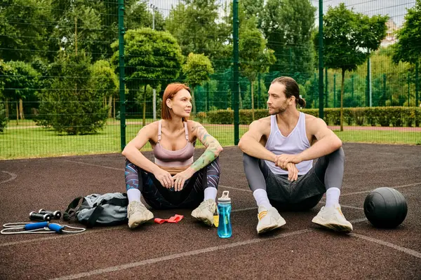 A woman, in sportswear, sit on a basketball court, guided by a personal trainer with determination and motivation. — Stock Photo