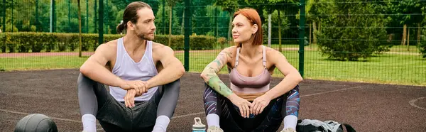 Определенный мужчина и женщина в спортивной одежде сидят на баскетбольной площадке, демонстрируя свою преданность фитнесу. — стоковое фото