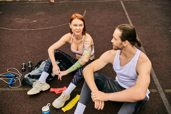 Un uomo e una donna in abbigliamento sportivo, che riposano su un campo da basket, trasudando determinazione e motivazione. — Foto stock