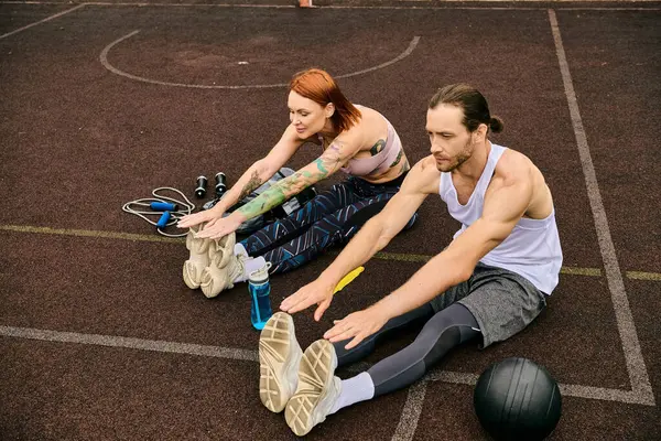 Un uomo e una donna in abbigliamento sportivo siedono su un campo da basket, concentrati sul loro allenamento insieme. — Foto stock