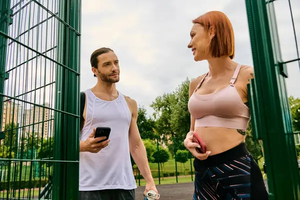 A man and woman in sportswear exercise together outdoors, holding smartphone — Stock Photo