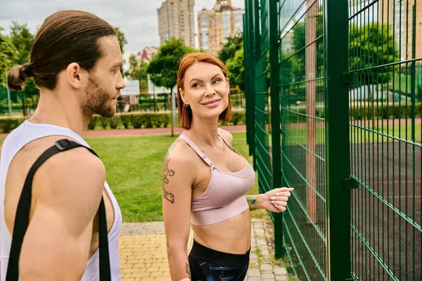 Ein Mann und eine Frau in Sportkleidung, die neben einem Zaun stehen und nach dem Sport im Freien Entschlossenheit und Motivation ausstrahlen — Stockfoto